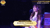 a woman named kizuna tanaka stands in front of a sign