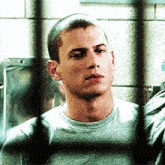 a close up of a man behind bars with a shaved head