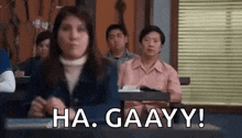 a group of people are sitting at desks in a classroom with a woman standing in front of them .