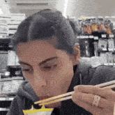 a woman is eating something with chopsticks and a ring on her finger