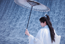 a man with long hair is holding a large umbrella in front of a waterfall