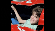 a boy is sitting in a red race car with the word hud on the side