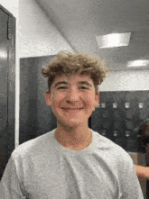 a boy with curly hair is smiling in front of lockers