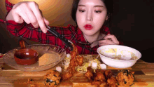 a woman in a plaid shirt is eating fried chicken with tongs