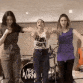 three women are dancing in front of a drum set with the word the warn on it .