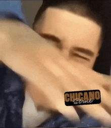 a close up of a man covering his face with his hand with a sticker that says chicano