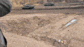 two military tanks are parked in a dirt area