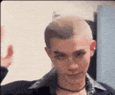 a man with a shaved head is wearing a choker and a shirt .