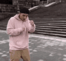 a man in a pink hoodie is standing in front of some stairs .
