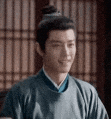 a man with a bun on his head is wearing a blue shirt and smiling .