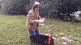 a woman in a hat is standing next to a fire pit holding a piece of paper