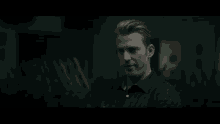 a man in a black shirt is standing in a dark room looking down .