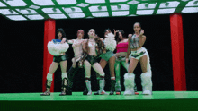 a group of women are standing on a green stage with a black background