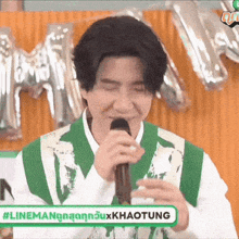 a young man is singing into a microphone while wearing a green vest .
