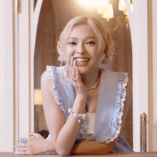 a woman in a blue dress is smiling with her hands on her chin
