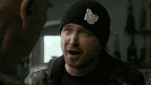 a man wearing a beanie is talking to another man in a room .