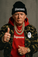 a man wearing a red supreme sweatshirt and a black beanie giving a thumbs up