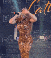 a woman in a leopard print jumpsuit is singing into a microphone in front of a wall that says dubai