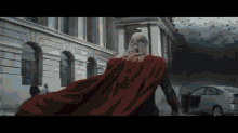 a man in a red cape is running in front of a building and a car .