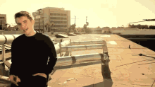 a man in a black shirt stands on a rooftop with his hands in his pockets