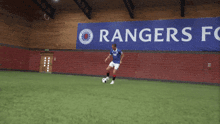 a man kicks a soccer ball in front of a rangers fc sign