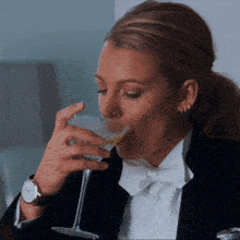 a woman wearing a tuxedo and bow tie drinks a martini