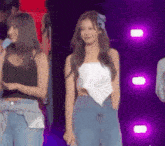 a woman in a white top and blue jeans is standing on a stage with a microphone .