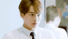 a young man in a white shirt and black tie is looking at himself in the mirror .