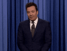 a man in a suit and tie is clapping in front of a curtain with a green button that says gyap
