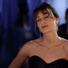 a woman in a black strapless dress and necklace is making a face .