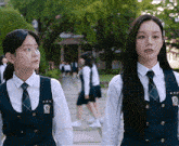 two girls wearing school uniforms and ties are standing next to each other on a sidewalk