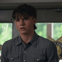 a young man in a striped shirt stands in front of a badge that says sheriff