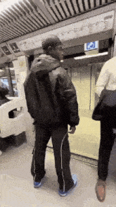 a man in a black jacket and black pants is standing in a subway car