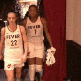 two female basketball players wearing fever uniforms are walking down a hallway