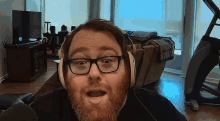a man with glasses and a beard wears headphones in a living room