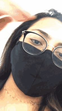 a woman wearing glasses and a black face mask looks at the camera