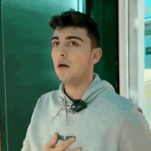 a young man in a hoodie is standing in front of a blackboard and making a surprised face .