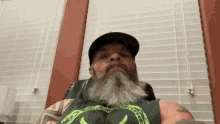 a man with a beard wearing a hat and a green tank top with a snake on it