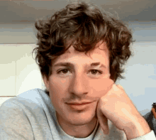 a close up of a man with curly hair holding his hand to his chin .