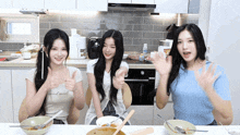 three girls are sitting at a table with bowls of food and one of them is wearing a shirt that says " thank you "
