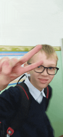 a young boy wearing glasses and a backpack giving the peace sign