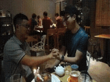 two men are sitting at a table holding hands in a dark room
