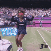 a woman is dancing on a tennis court with a sign that says v103 in the background