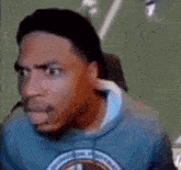 a man in a blue sweatshirt is sitting in a chair with a microphone in his ear .