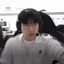 a man wearing headphones and a white adidas shirt looks at the camera