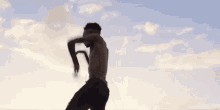 a man without a shirt is standing in front of a blue sky with clouds .