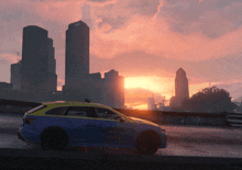 a blue and yellow downtown taxi cab is driving down a city street at sunset