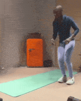 a man is jumping on a green mat in front of an orange refrigerator
