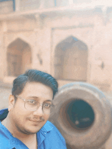 a man wearing glasses and a blue shirt stands in front of a large object