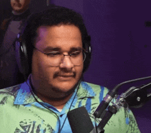 a man wearing glasses and headphones stands in front of a microphone with a purple background